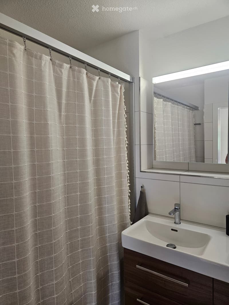 Modern bathroom with a white sink, chrome faucet, large mirror, and a beige shower curtain with a grid pattern.