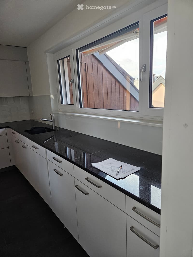 Modern kitchen with white cabinets, black countertops, and a sink. Papers and a pen are placed on the counter.
