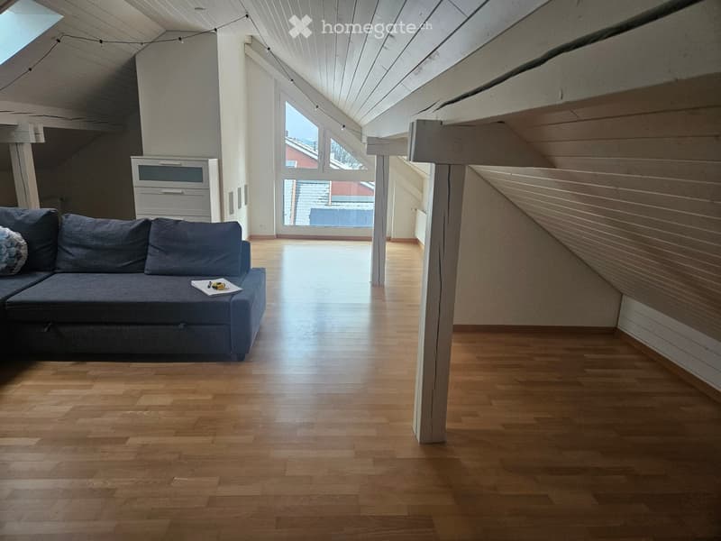 Bright living room with wooden flooring, a blue sofa, a small storage unit, and a table with papers and tools.