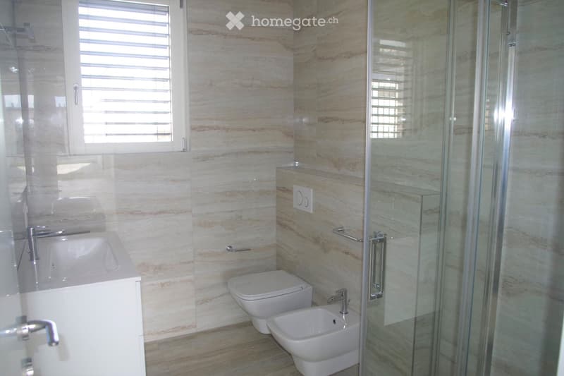 Modern bathroom with marble-style walls, a bathtub, toilet, bidet, and a glass-enclosed shower stall.