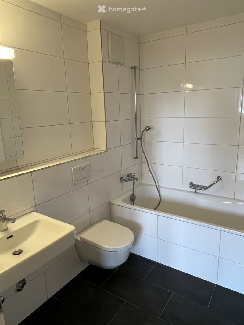 A bathroom with white tiles, a bathtub, a toilet, a sink, and a mirror.