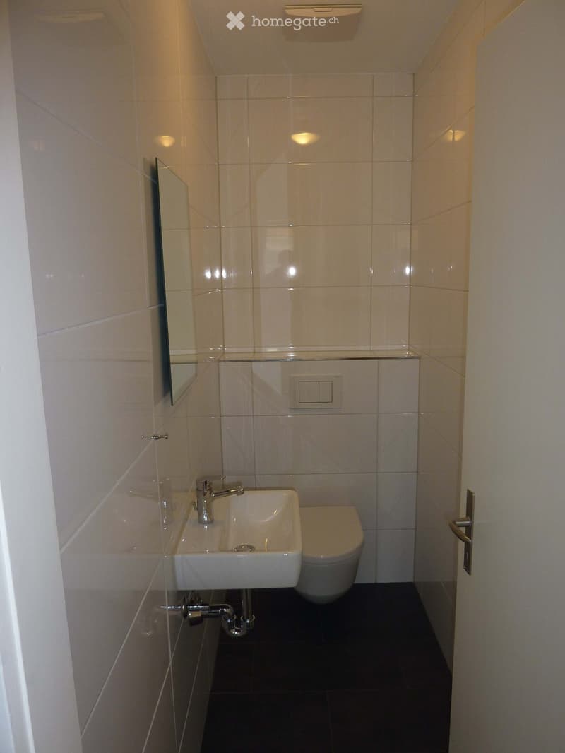 Modern bathroom with white tiles, a white sink, a chrome faucet, a toilet, and a mirror on the wall.