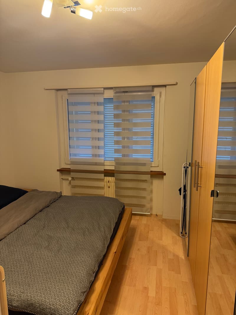 Cozy bedroom with a wooden bed, grey patterned bedding, a radiator, and a wardrobe with mirrored doors.