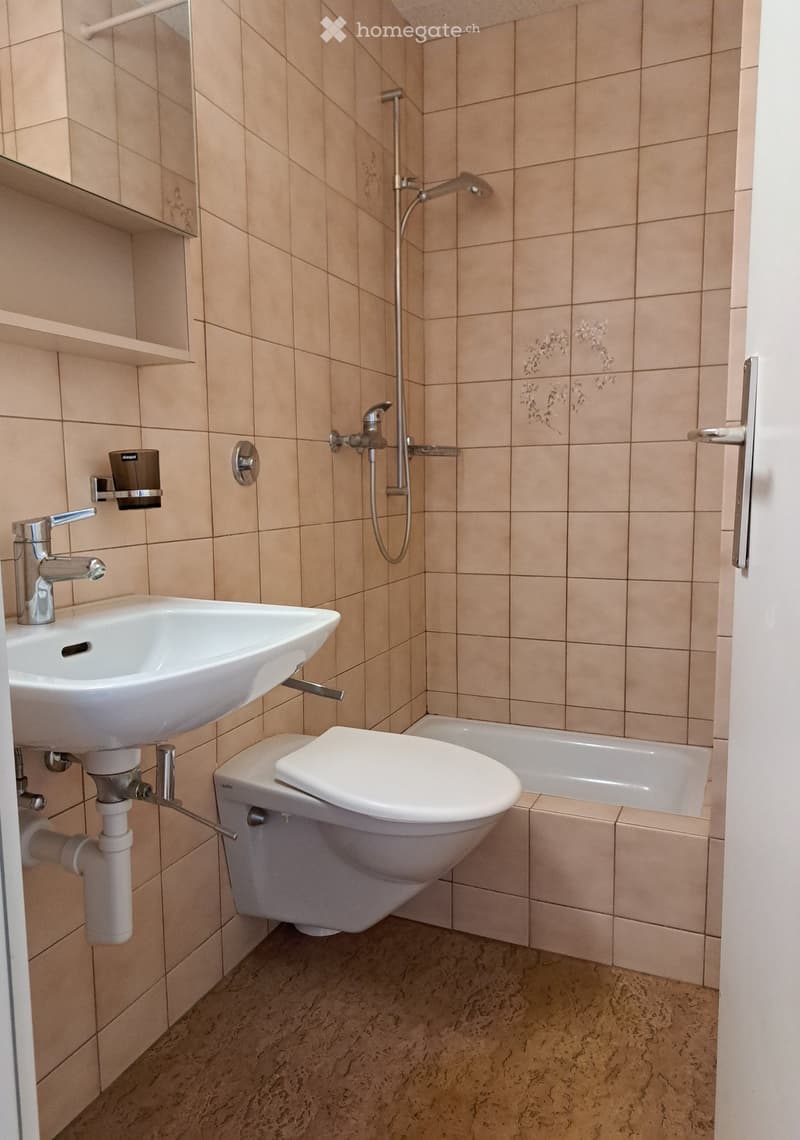 Modern bathroom with beige tiles, a white sink, toilet, bathtub, and a showerhead with a handheld sprayer.