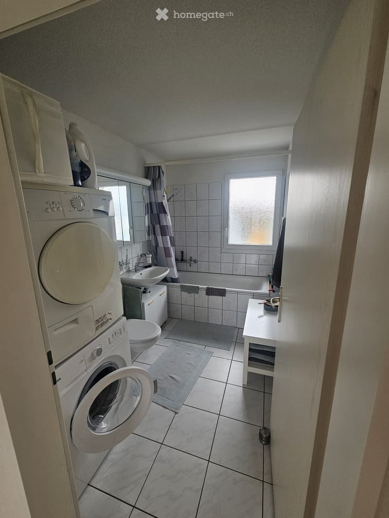 Bathroom with a washing machine, sink, toilet, bathtub, and a small table with a towel.