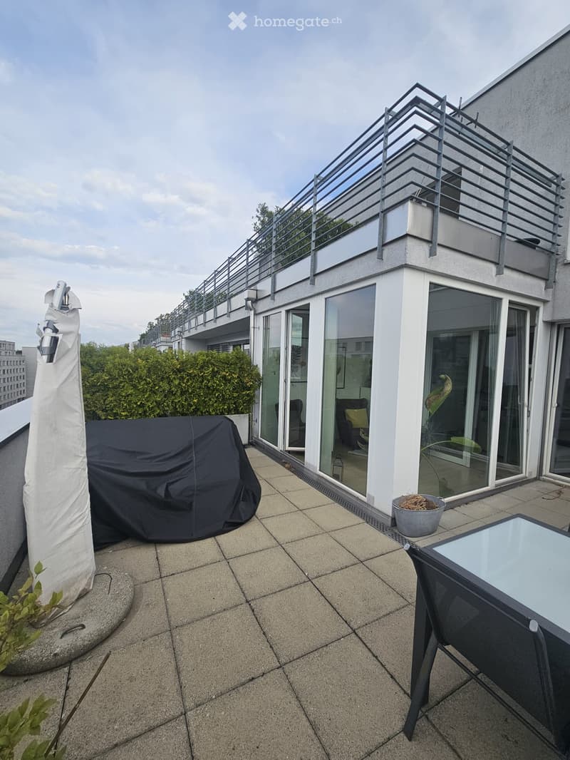Modern rooftop terrace with tiled floor, glass sliding doors leading to interior, covered furniture, potted plants, and a small table and chair set.