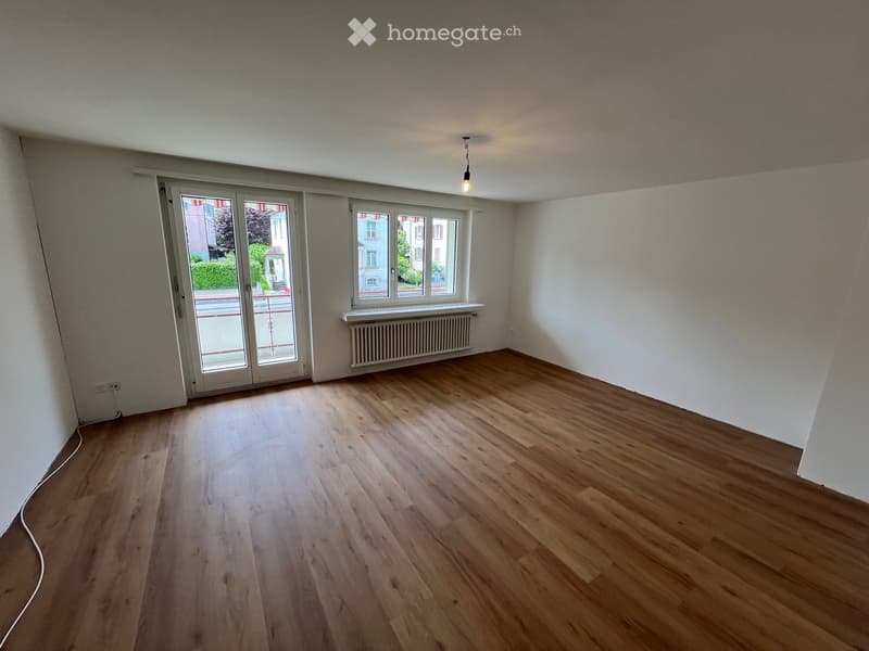 Empty room with wooden flooring, white walls, large windows, and a radiator. No furniture or equipment present.