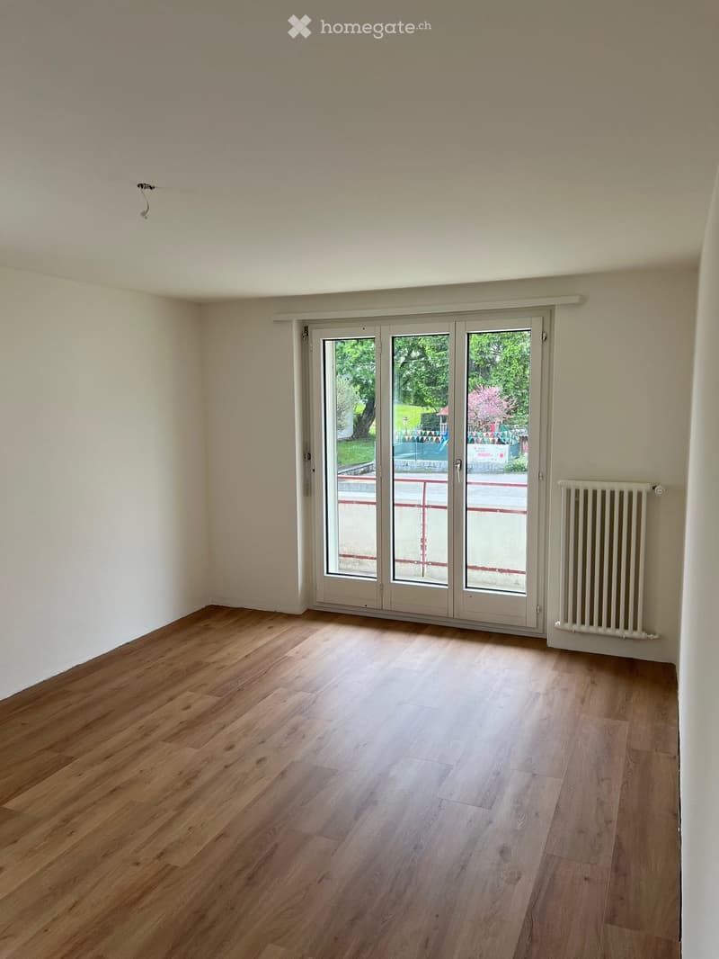 Empty room with wooden flooring, white walls, large sliding glass doors, and a radiator on the right side.