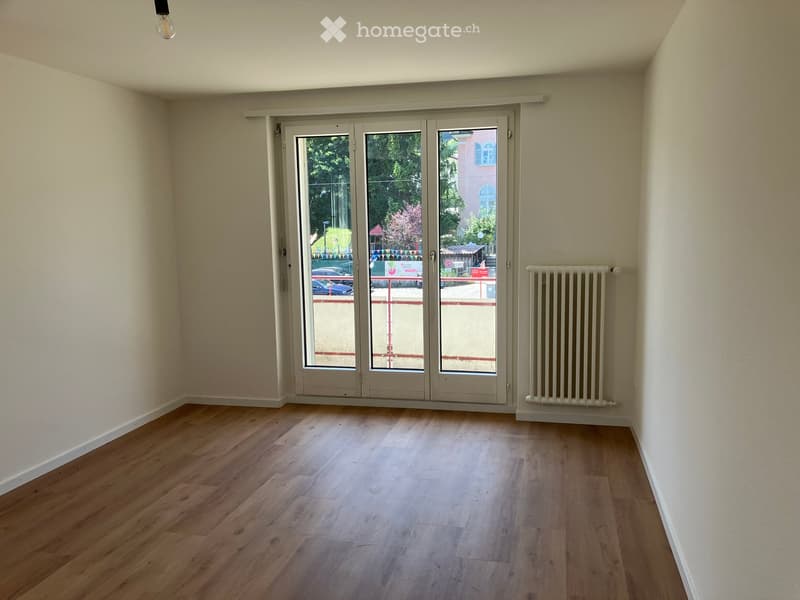 Empty room with wooden flooring, large sliding glass doors, and a radiator on the wall.