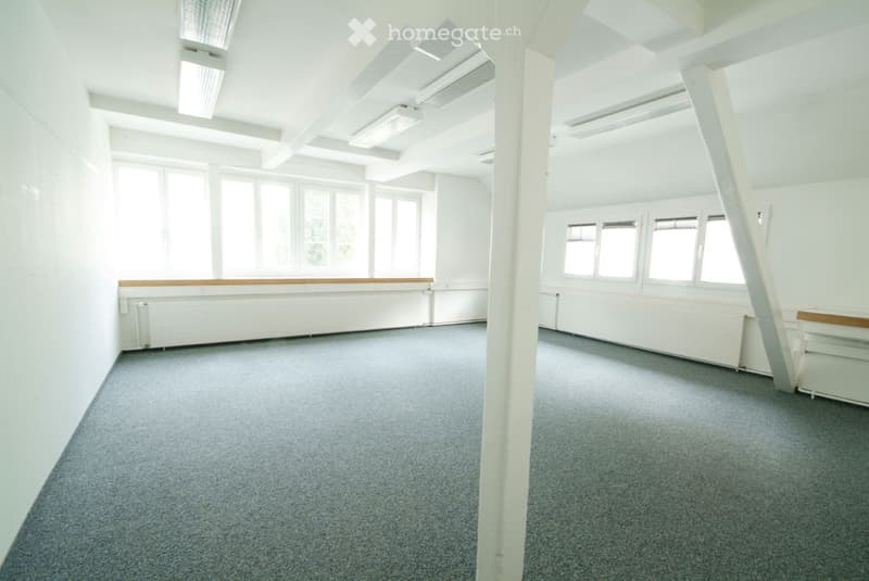 Empty room with white walls, grey carpet, large windows, and exposed ceiling beams.