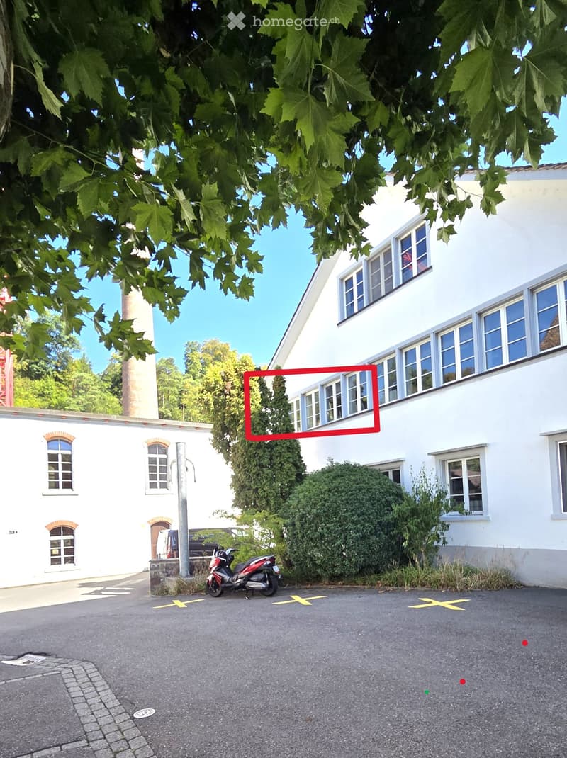 Two-story white building with multiple windows, surrounded by greenery and a parked scooter.