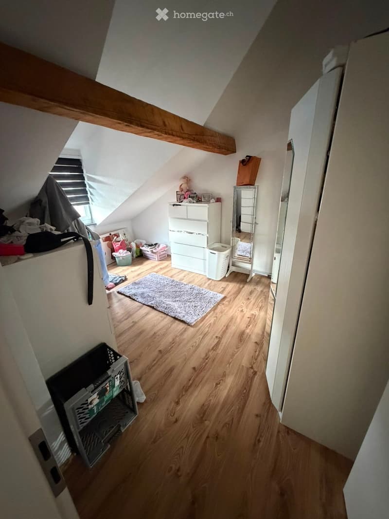 Attic room with wooden flooring, slanted ceiling, and skylight window. Contains a chest of drawers, mirror, rug, laundry baskets, and some toys.
