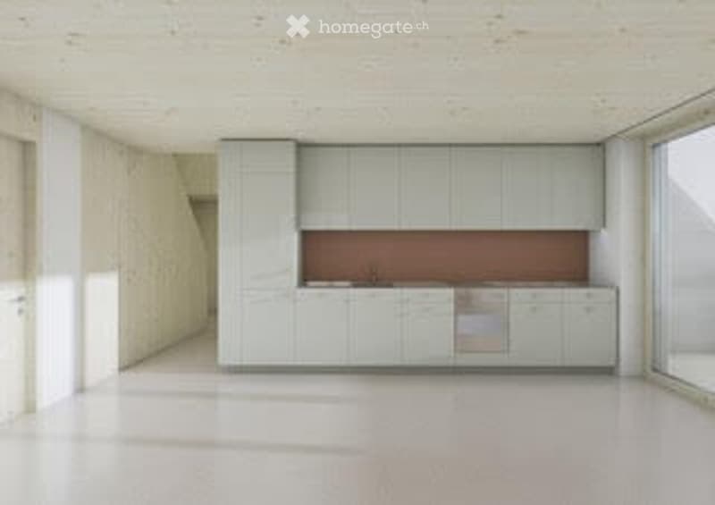 Modern, minimalist kitchen with white cabinetry, a stainless steel dishwasher, and a light-colored countertop. The space is unfurnished and empty, with large windows allowing natural light to fill the room.