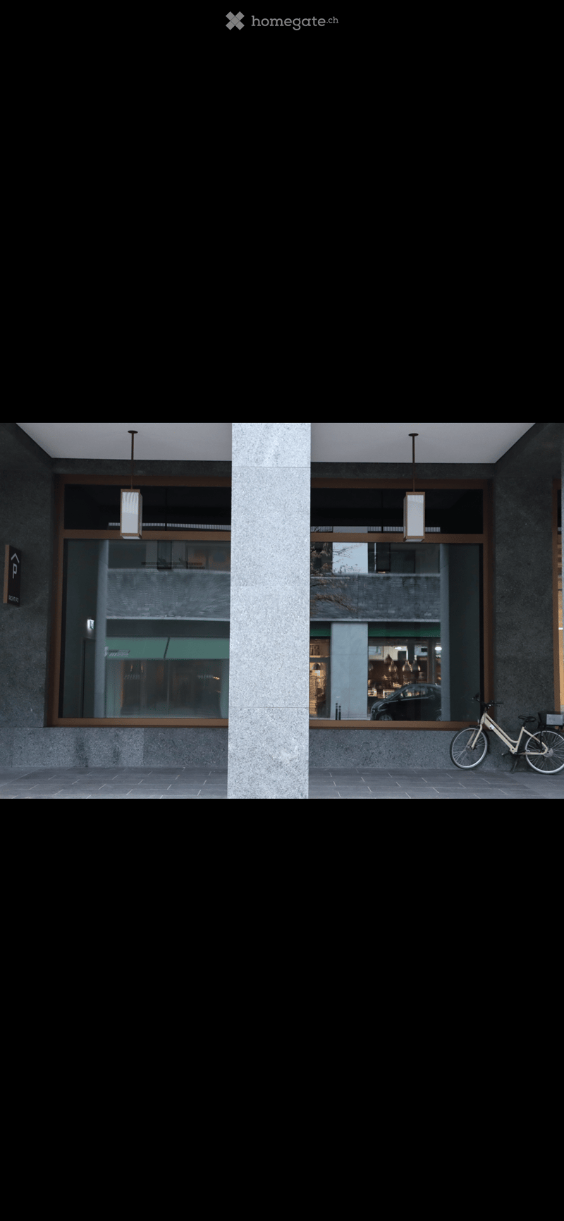Modern building entrance with large glass windows, hanging pendant lights, and a bicycle parked outside.