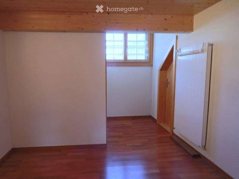 Empty hallway with wooden flooring, white walls, and a window with decorative glass at the far end. A door is visible on the right side.
