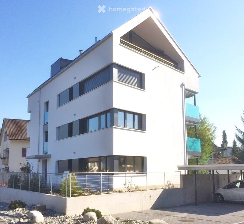 Modern two-story house with white exterior, large windows, and a garage. Features a raised ground floor and contemporary design.