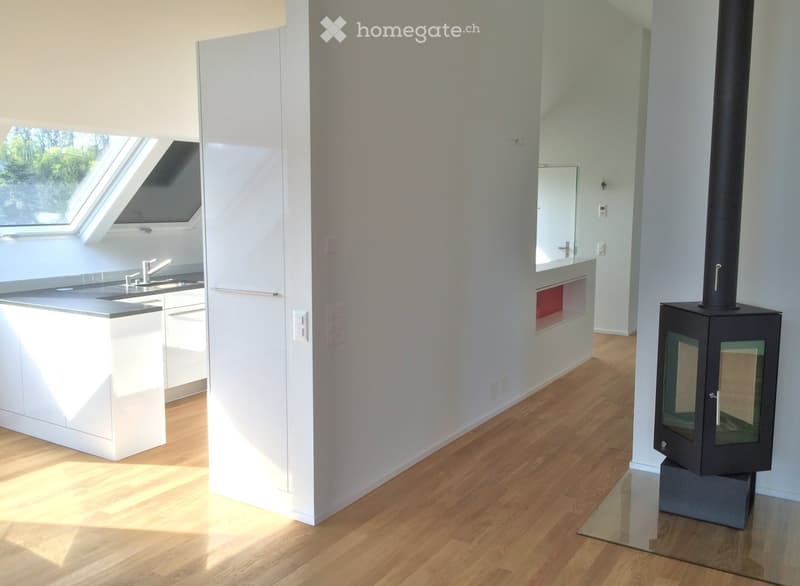 Modern kitchen with white cabinets, a central island, and a sleek black wood-burning fireplace with a glass front.