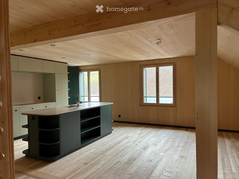 Modern kitchen with light wood walls and ceiling, wooden flooring, central island with sink and faucet, and light green cabinets.