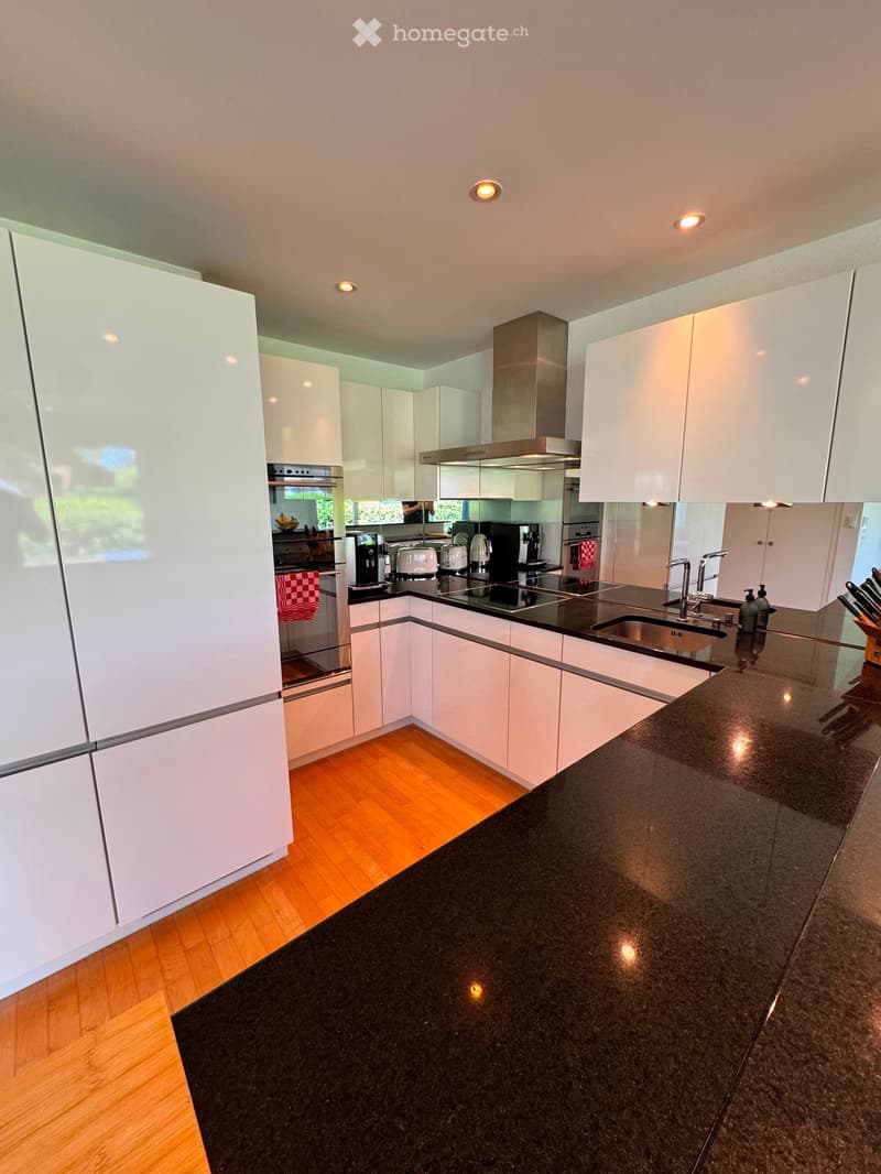 Modern kitchen with white cabinets, black granite countertop, stainless steel appliances, and wooden flooring.