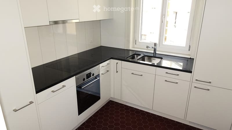 Modern kitchen with white cabinets, black countertops, stainless steel sink, and built-in oven.