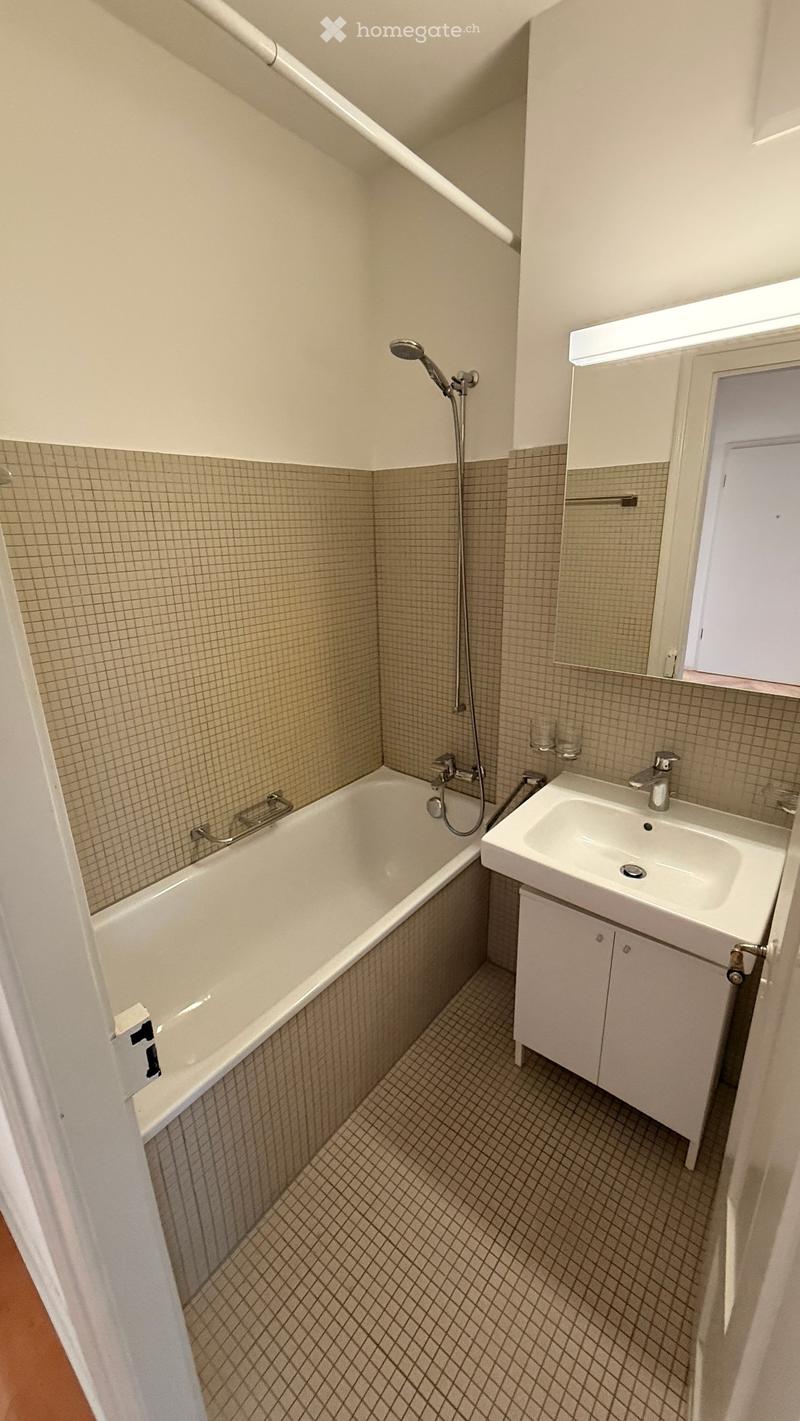 Modern bathroom with a bathtub, sink, and mirror. Features tiled walls and a small window for natural light.