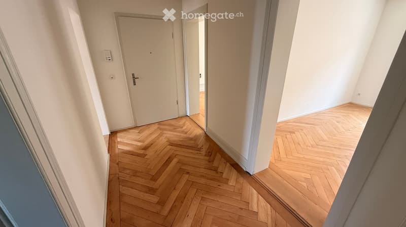 Empty hallway with wooden herringbone flooring, white walls, and two closed doors.