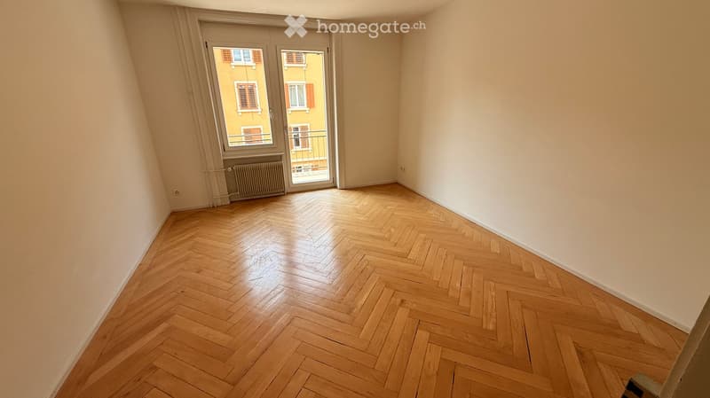 Empty room with wooden herringbone flooring, white walls, and a large glass door leading to a balcony.