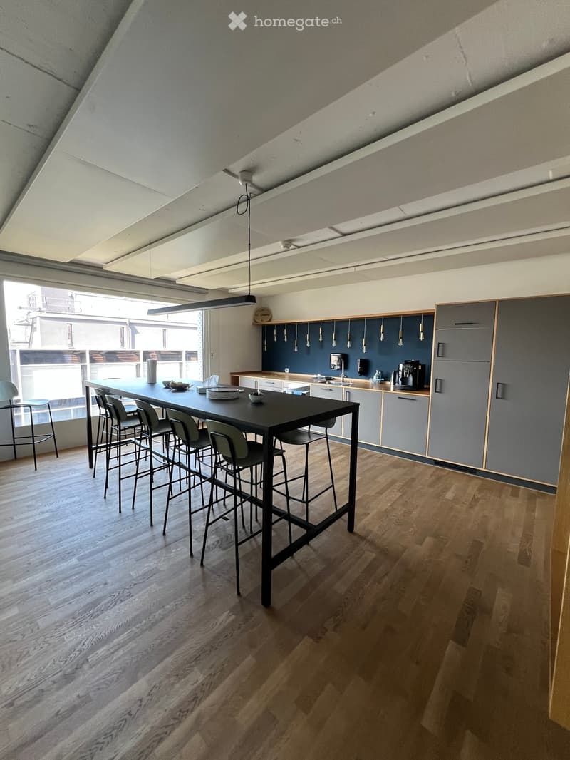 Modern kitchen with wooden flooring, grey cabinets, a black dining table surrounded by chairs, and a coffee machine on the counter.