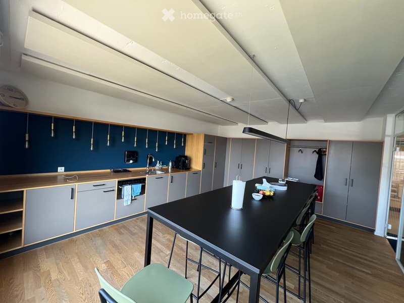Modern kitchen with grey cabinets, wooden countertops, and a black island table with chairs. Features include a sink, oven, microwave, coffee maker, and various small appliances.