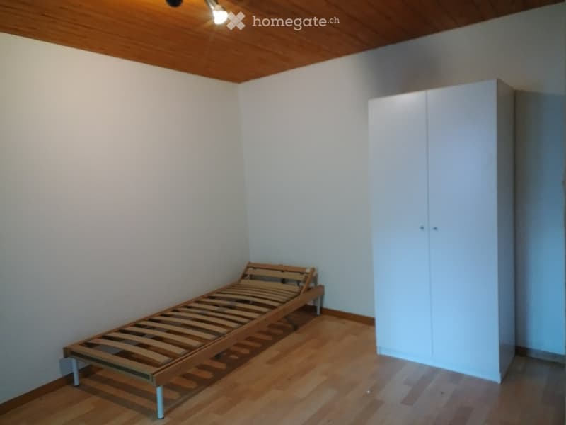 A small bedroom with wooden flooring, white walls, a wooden bed frame, and a white wardrobe.
