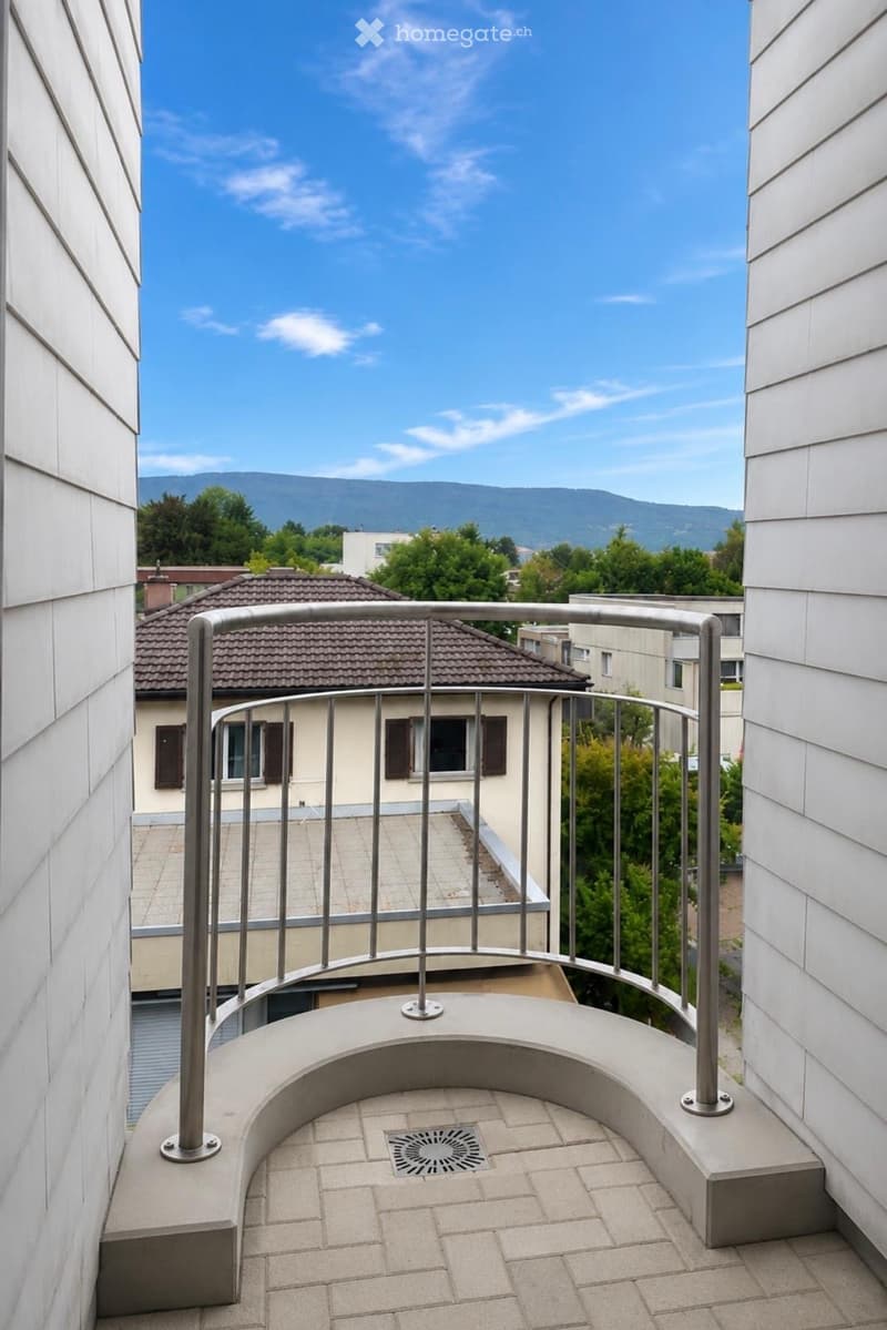 Balcony with metal railing, tiled floor, and a scenic view of a town and mountains in the background.