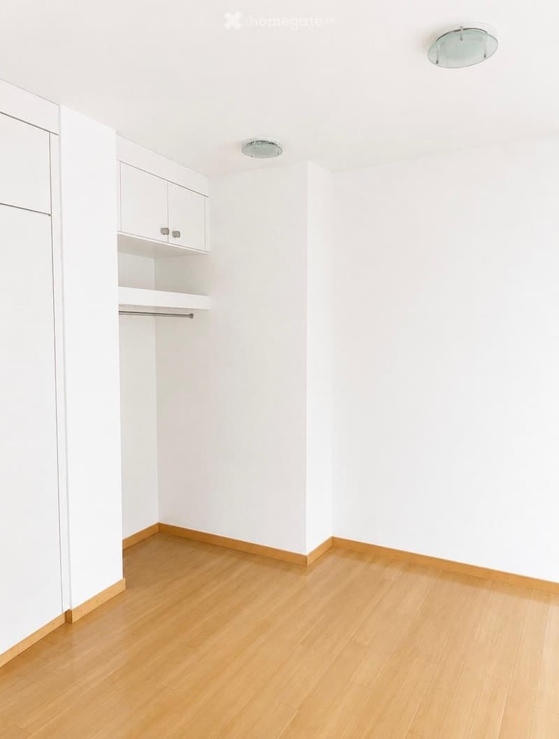 Empty room with white walls, light wooden flooring, built-in closet with shelves, and recessed ceiling lights.
