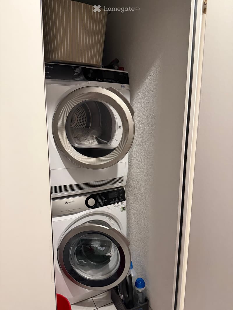 A compact bathroom with a stacked washing machine and dryer unit, featuring a control panel and a small shelf above.