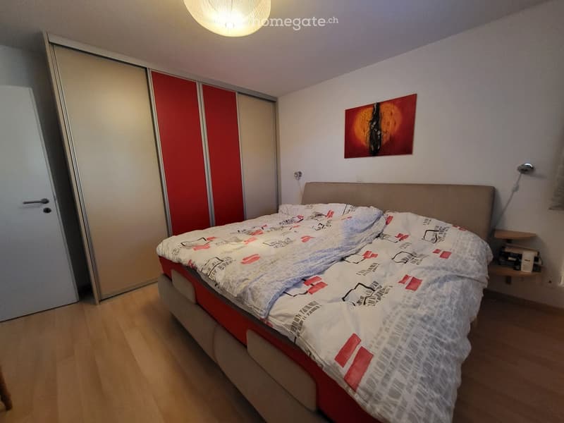 Bedroom with a double bed, nightstand, and a painting on the wall. The room features wooden flooring and a sliding closet.
