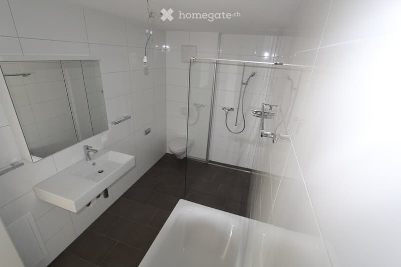 Modern bathroom with white tiles, a white sink, a large mirror, a toilet, a bathtub, and a glass-enclosed shower area.