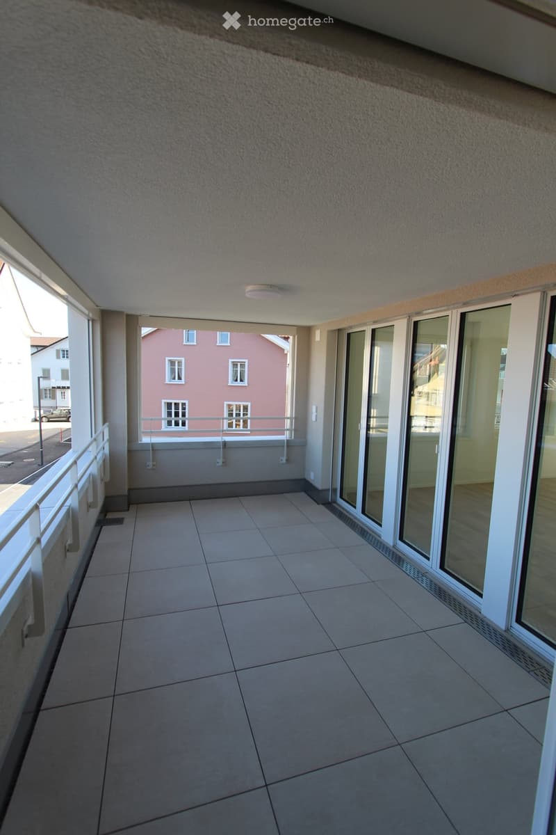 Empty balcony with tiled floor, white railing, and sliding glass doors leading to the interior.
