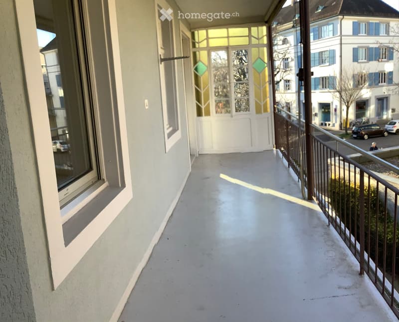 Balcony with white floor, metal railing, and large windows with decorative glass panels.