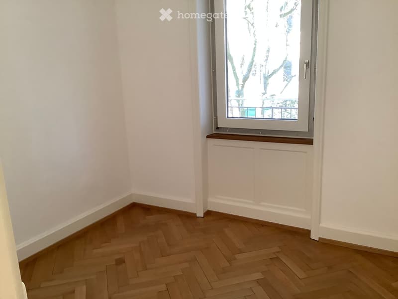 Empty room with wooden herringbone flooring, white walls, and a window with a wooden sill.