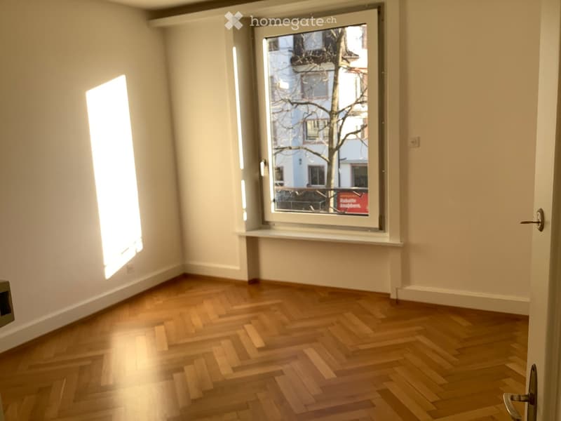 Empty room with wooden flooring, white walls, and large windows letting in natural light.