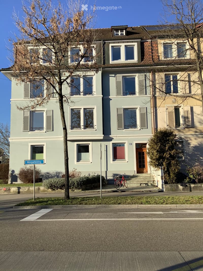 Two-story residential building with light blue and beige facade, multiple windows, and a bicycle parked in front.