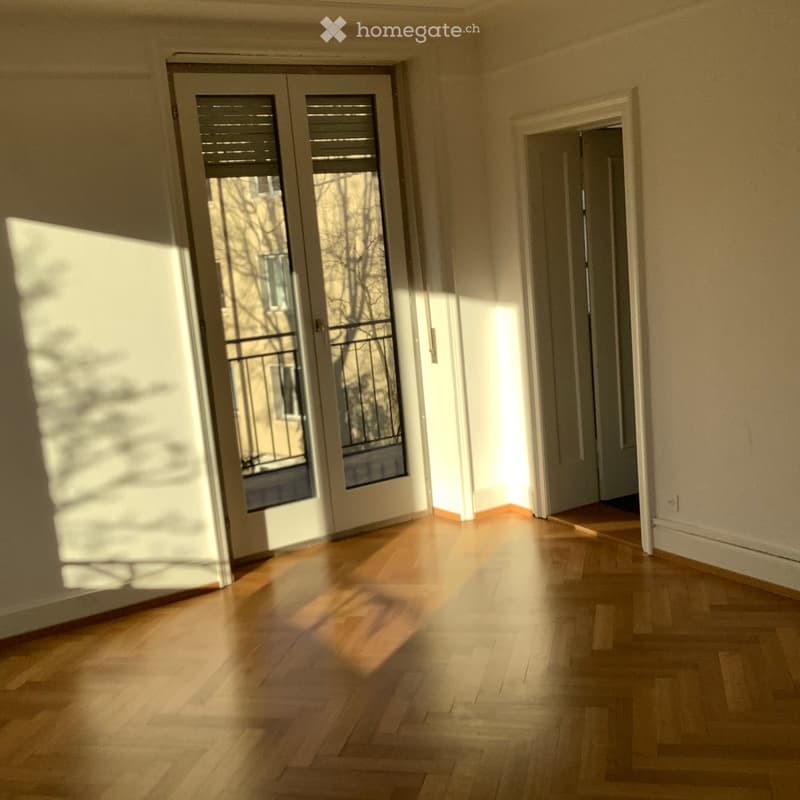 Empty hallway with wooden flooring, large sliding glass doors leading to a balcony, and a doorway to another room.