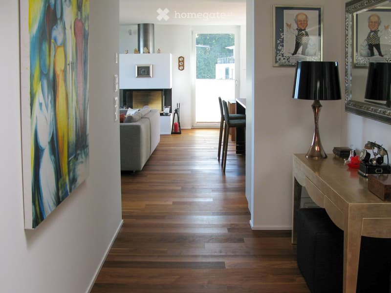 Modern living room with hardwood floors, a grey sofa, a small table with chairs, a lamp, and artwork on the walls.