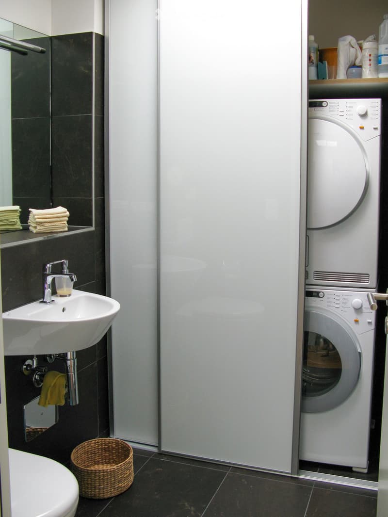 Modern bathroom with a white sink, chrome faucet, mirror, towels, wicker basket, and a stacked washer/dryer unit.