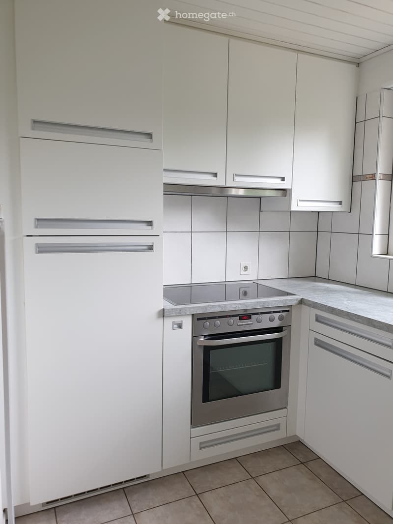 Modern kitchen with white cabinets, stainless steel oven, and tiled floor.