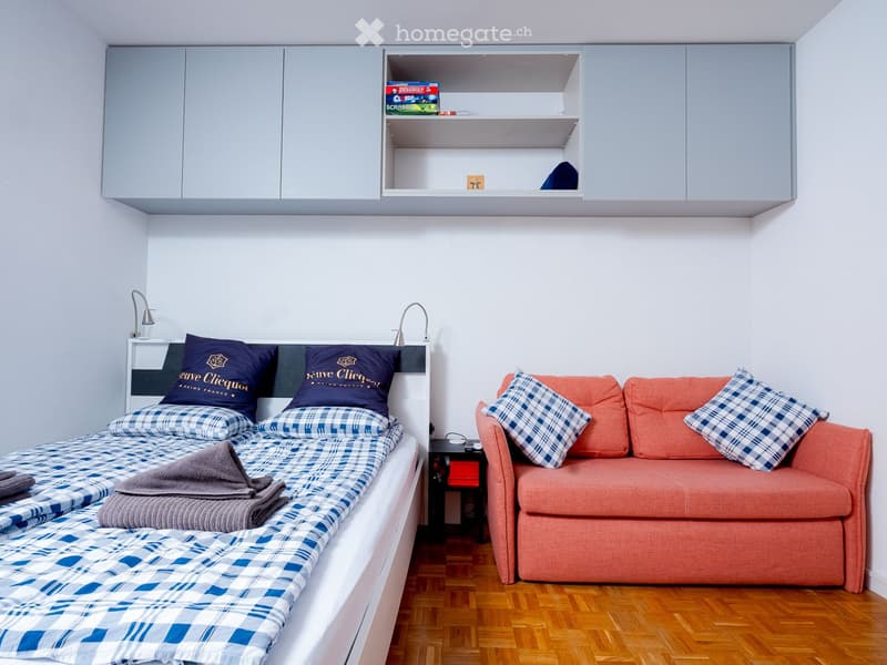 A room with twin beds, an orange couch, nightstand, and built-in cabinets.