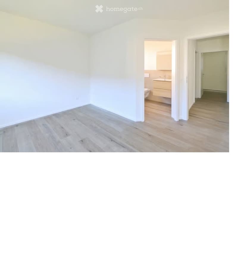 Empty room with light wooden flooring and white walls, featuring an open doorway leading to a small bathroom with a sink and toilet.