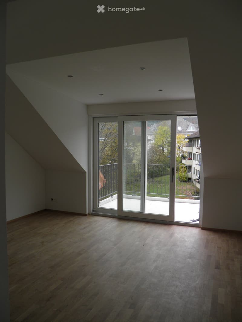 Empty room with wooden flooring and large sliding glass doors leading to a balcony or terrace. The ceiling has a sloped design typical of an attic space.