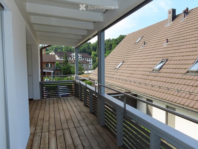 Balcony with wooden decking, metal railings, and a view of neighboring houses and greenery.