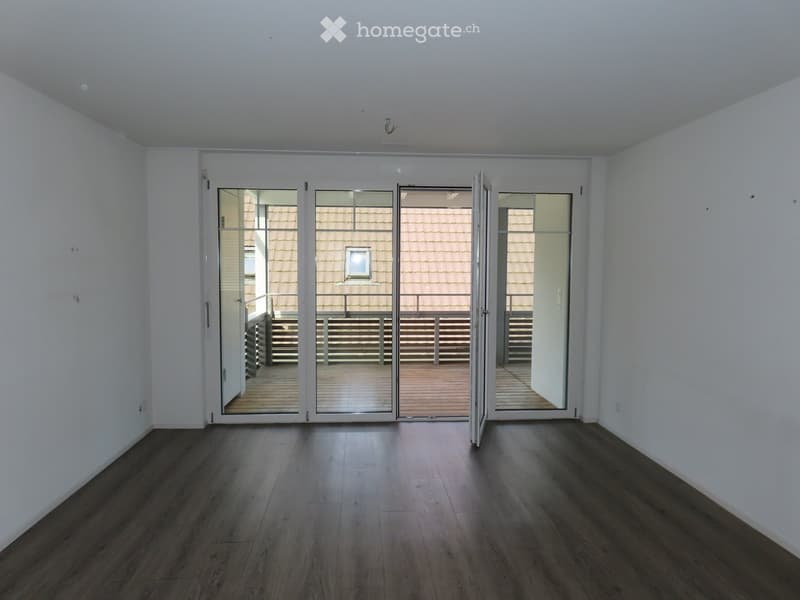 Empty room with dark wooden flooring and white walls, featuring large sliding glass doors that open to a wooden deck and outdoor area.