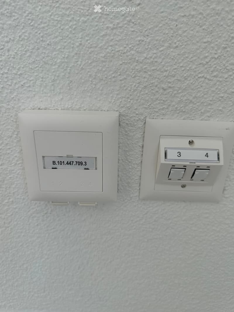 Two light switches mounted on a textured white wall, one labeled with a code and the other with numbers3 and 4.